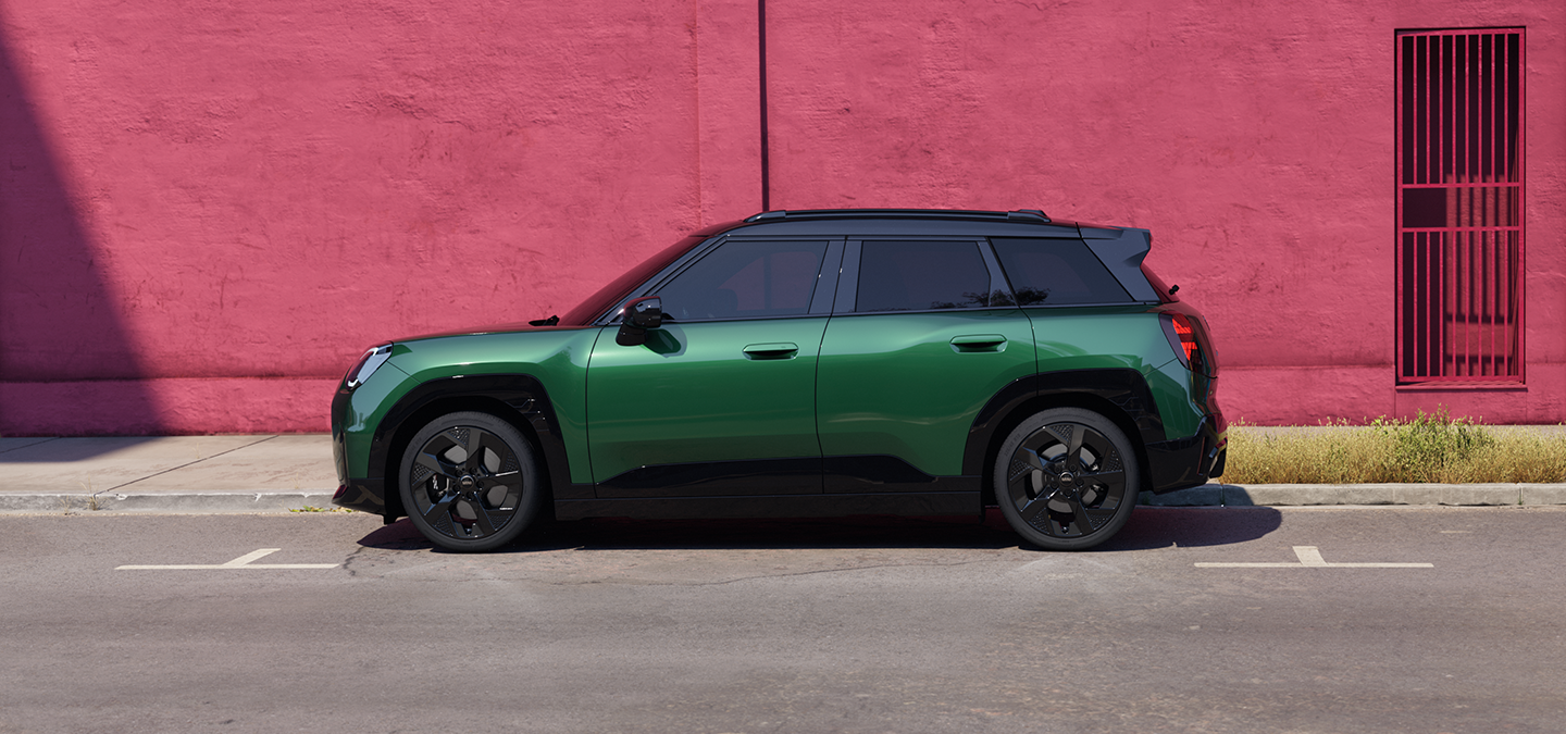 Seitenansicht des vollelektrischen MINI Aceman in British Racing Green mit schwarzem Dach auf einer Straße.
