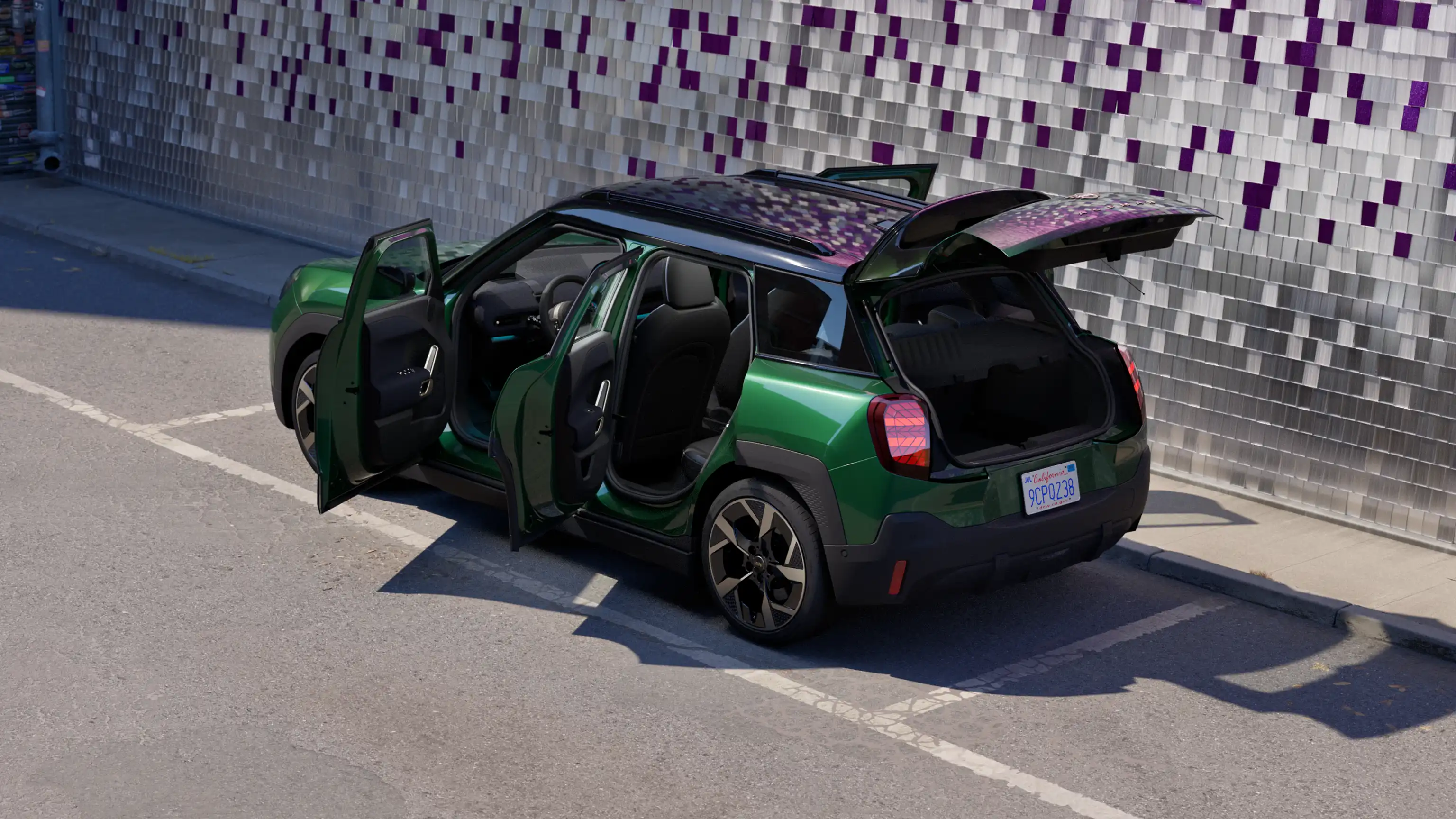 Seitliche Heckansicht eines vollelektrischen MINI Aceman in British Racing Green mit geöffneten Türen, der auf einem Parkplatz parkt, mit einer farbigen Wand im Hintergrund