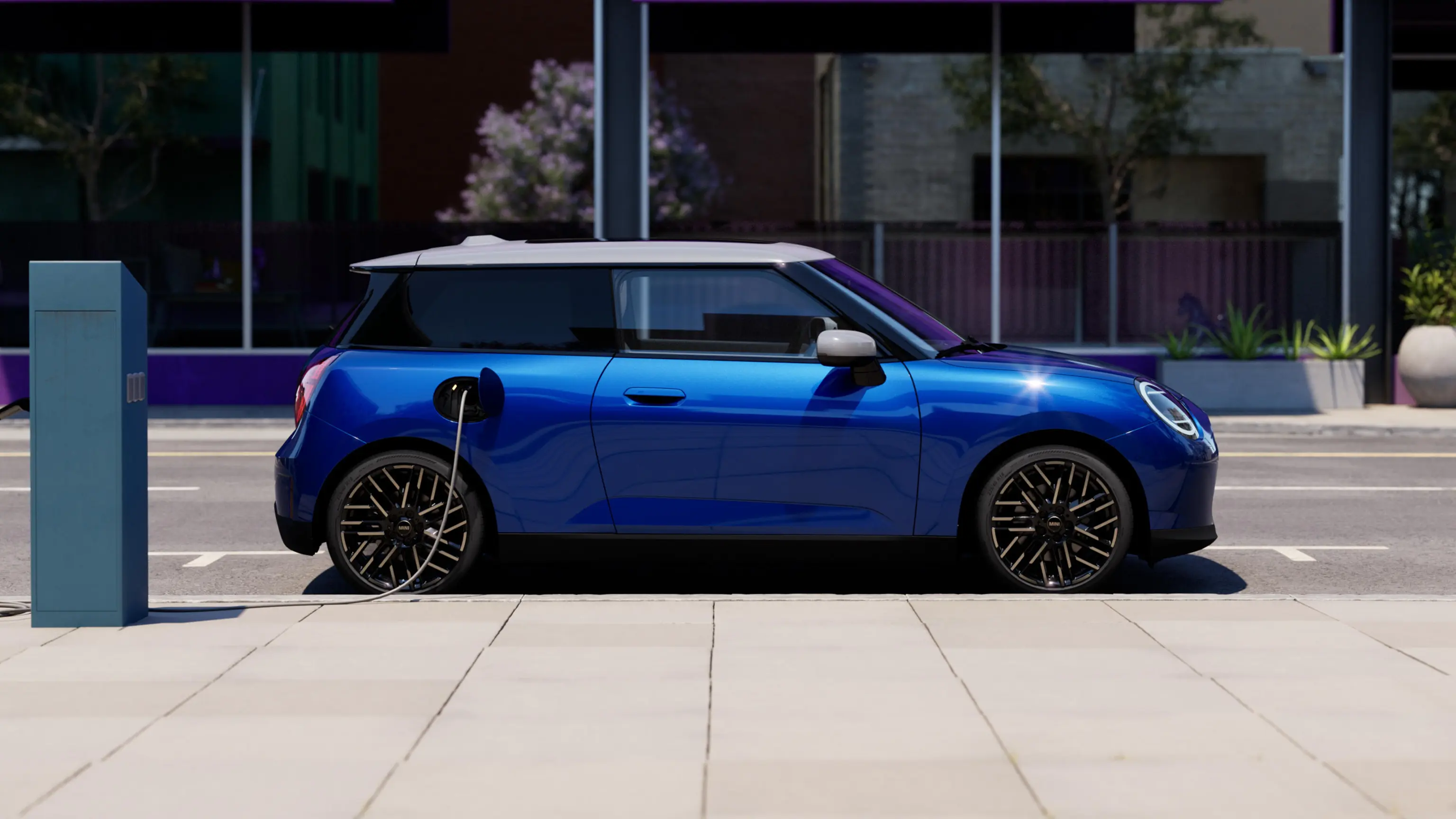 Seitenansicht eines vollelektrischen MINI Cooper in Blazing Blue, der auf dem Gehweg neben einer Ladestation parkt