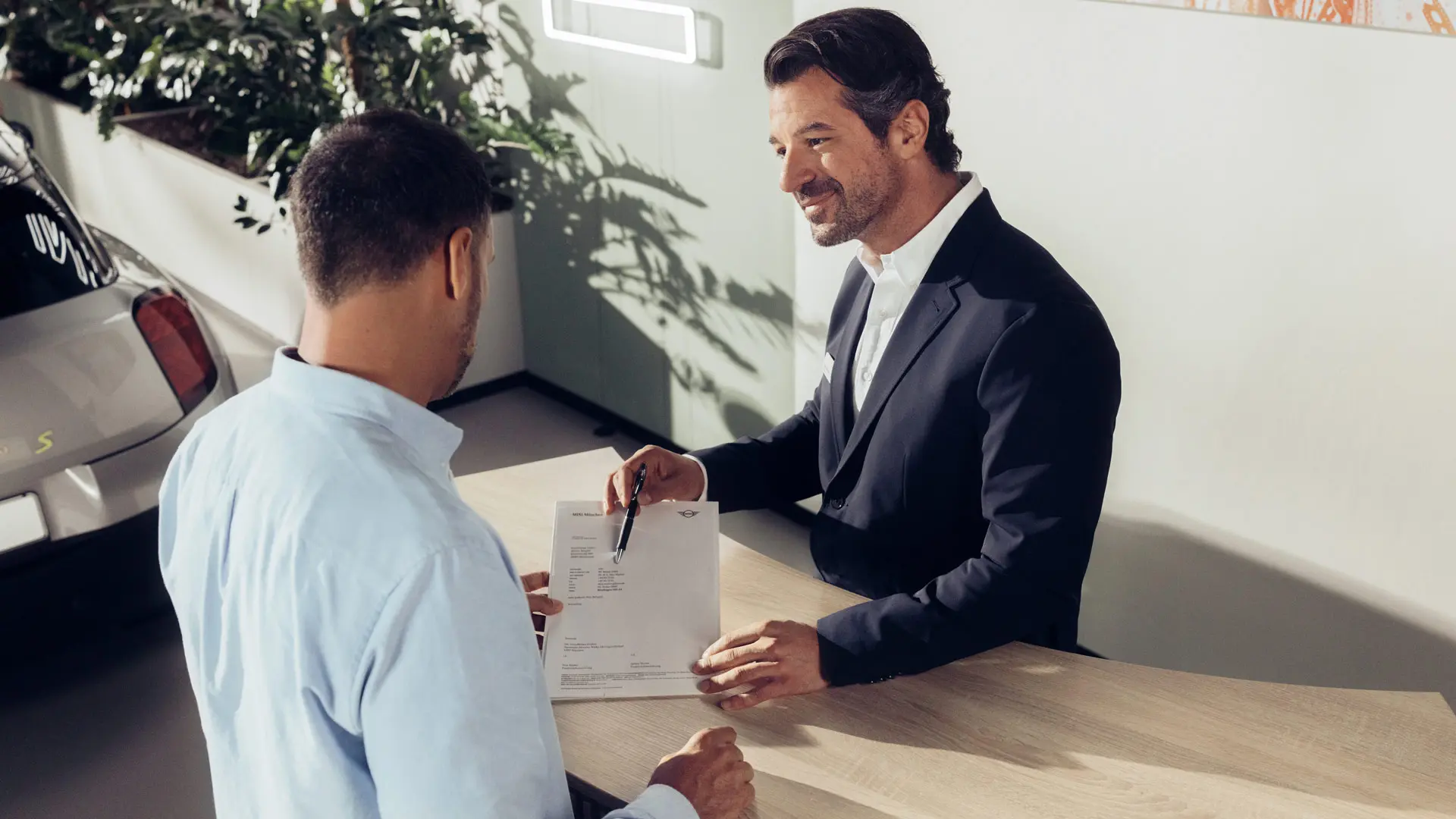 Ein Service Assistent bei einem MINI Partner berät einen Kunden über die Optionen der MINI Reifenversicherung.