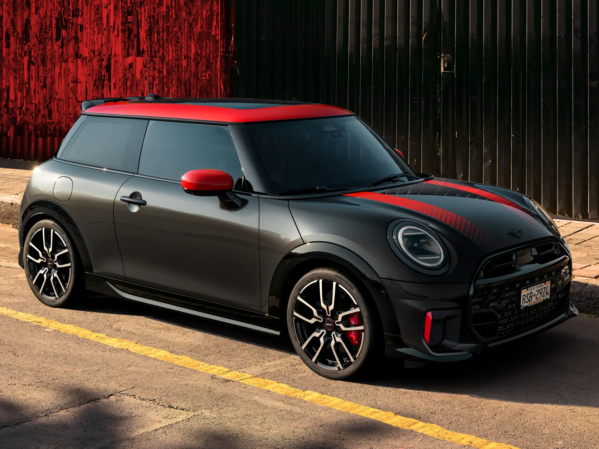 Seitenansicht eines MINI John Cooper Works 3-Türer in Midnight Black mit Dach und Spiegelkappen in Chili Red und roten Seitenstreifen, der am Straßenrand parkt.