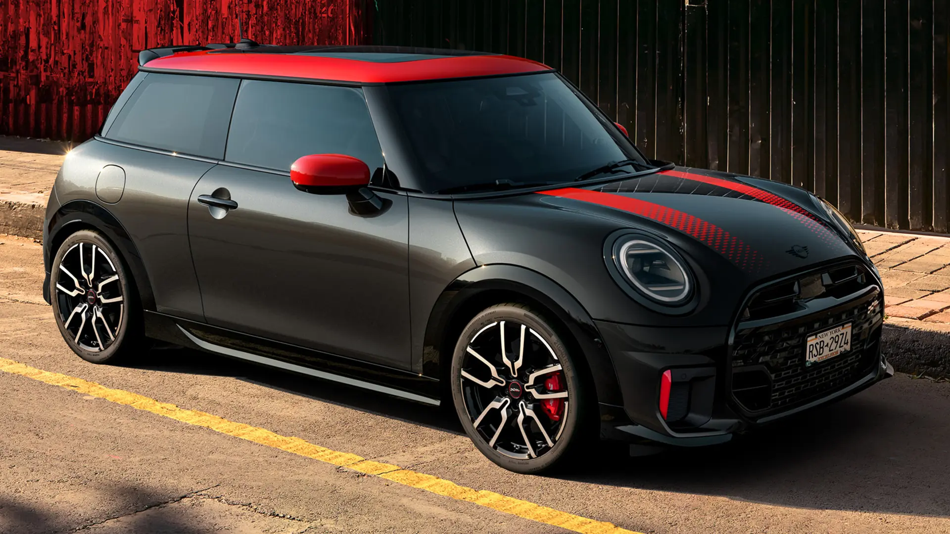 Seitenansicht eines MINI John Cooper Works 3-Türer in Midnight Black mit Dach und Spiegelkappen in Chili Red und roten Seitenstreifen, der am Straßenrand parkt.