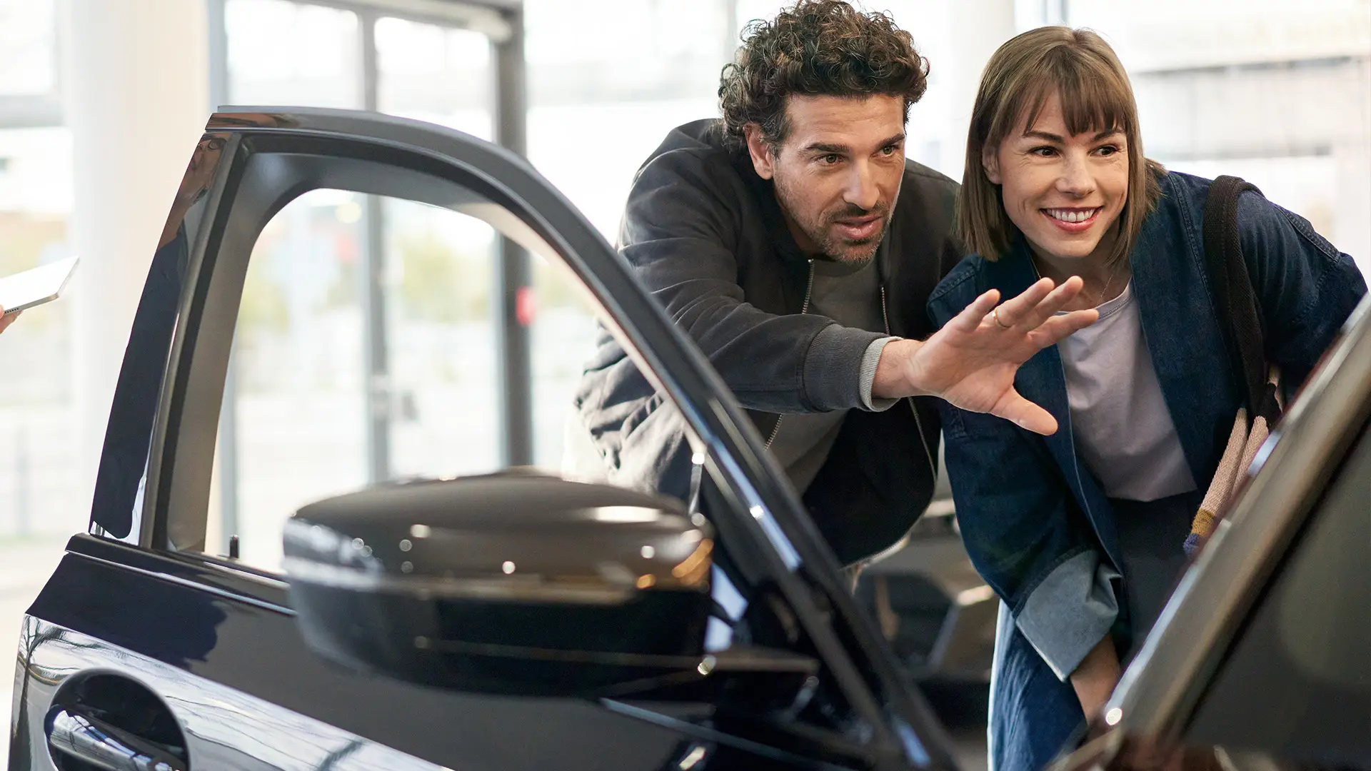 Ein MINI im Ausstellungsraum bei einem MINI Partner mit einem Berater, der einem Kunden die Innenausstattung zeigt.