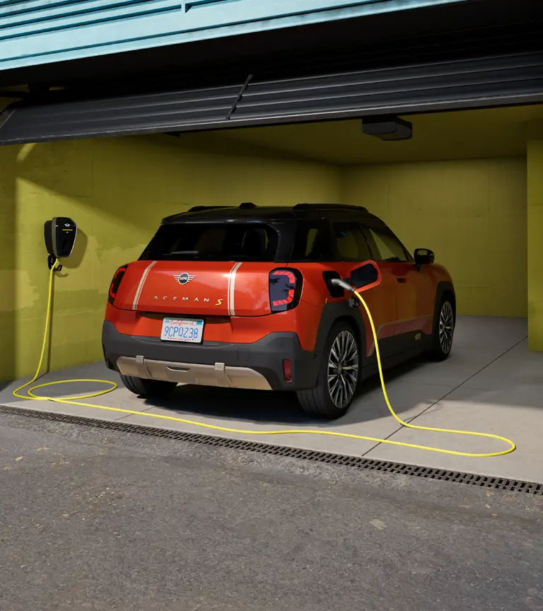 Heckansicht eines vollelektrischen MINI Aceman, der in einer Garage parkt und mit der MINI Wallbox Plus geladen wird.