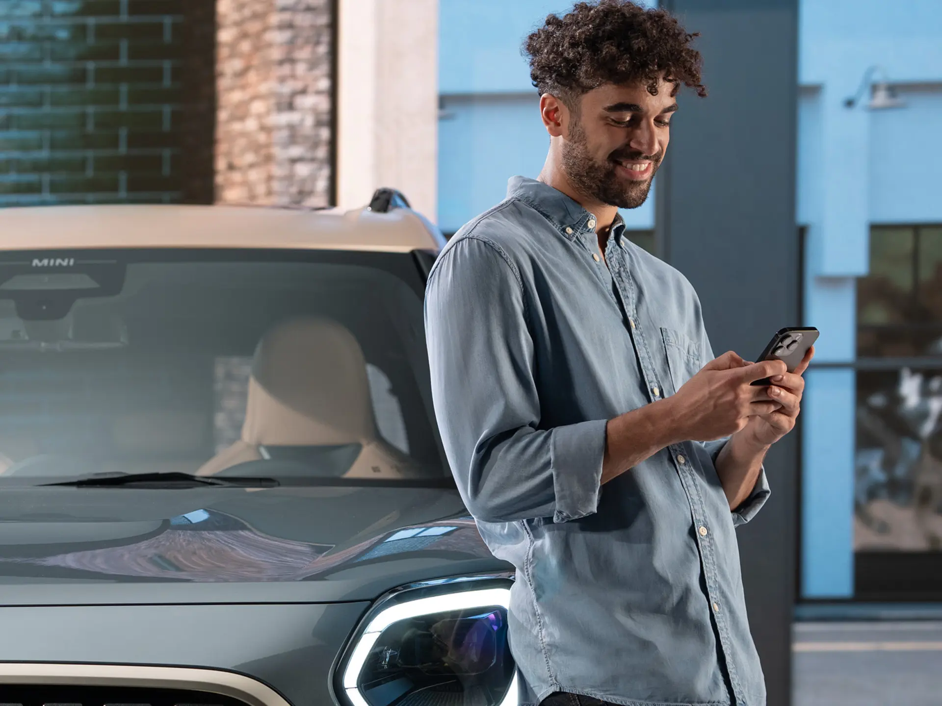 MINI personalisierte Service Termine –  ein Mann, der neben einem MINI auf seinem Handy tippt.