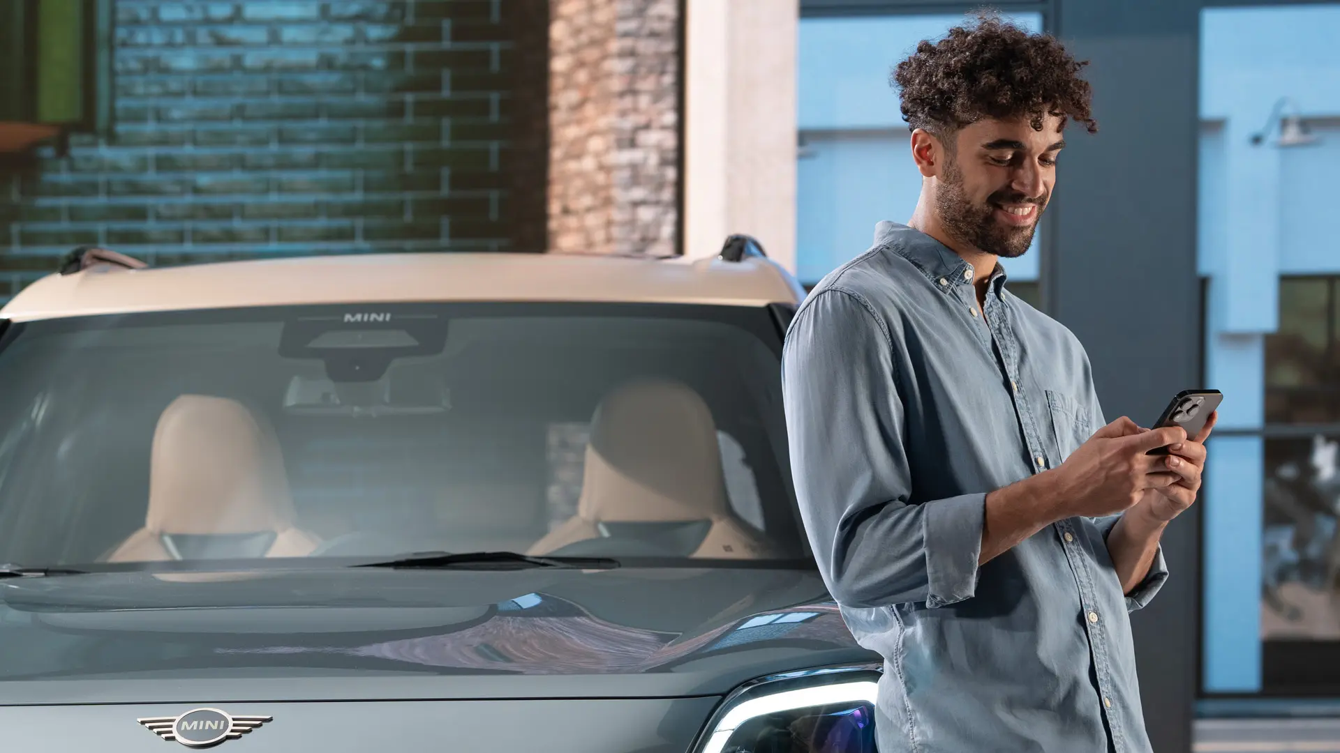 MINI personalisierte Service Termine – ein Mann, der neben einem MINI auf seinem Handy tippt.