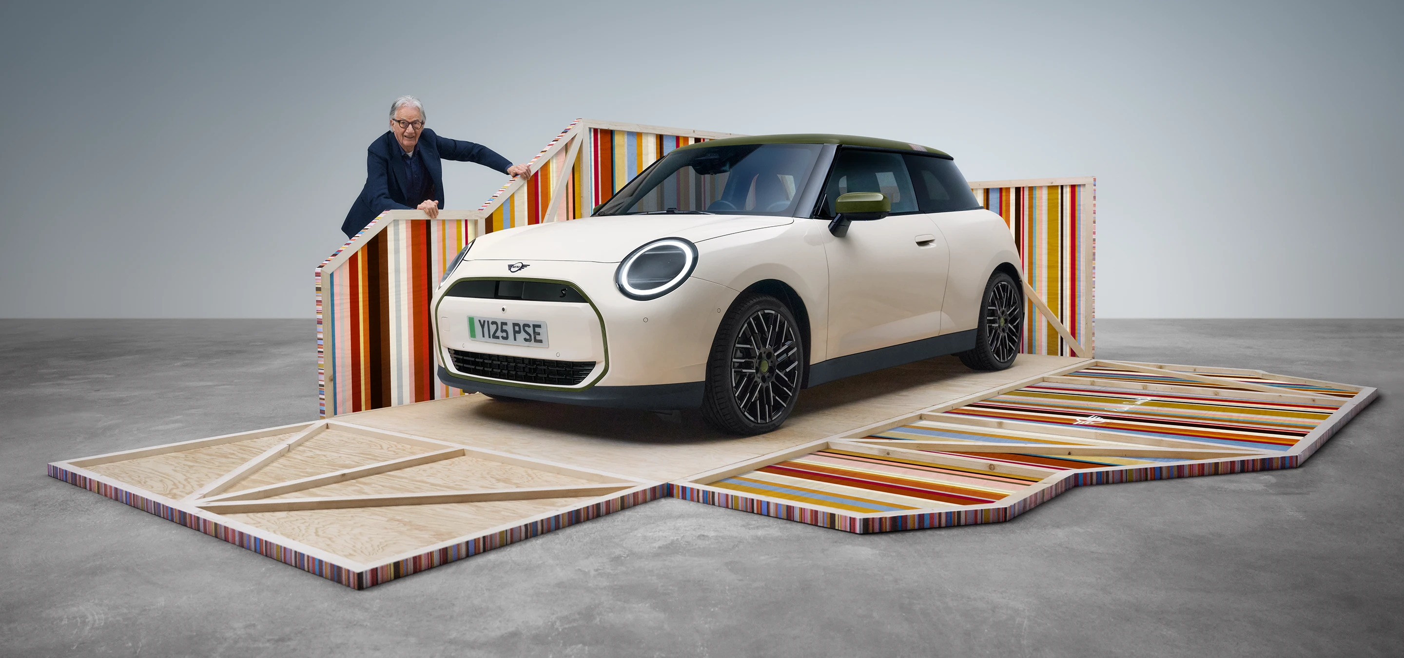 Frontansicht des vollelektrischen MINI Cooper Paul Smith Edition in Inspired White mit dem Designer Paul Smith