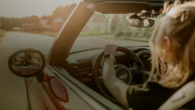 Eine Frau fährt bei Sonnenuntergang mit heruntergelassenen Fenstern in einem MINI Cabrio.