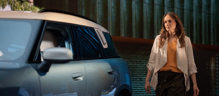 Eine junge Frau geht auf einen MINI Countryman zu Eine junge Frau geht auf einen MINI Countryman zu