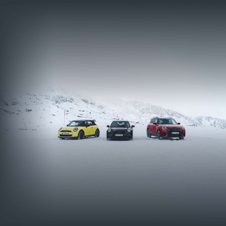 Drei MINI Fahrzeuge stehen nebeneinander auf einer verschneiten Fläche vor winterlicher Berglandschaft.