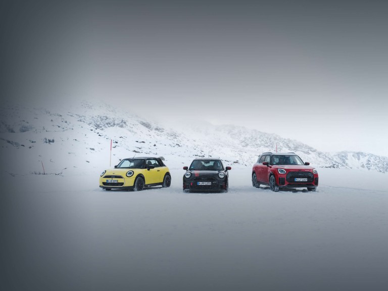Drei MINI Fahrzeuge stehen nebeneinander auf einer verschneiten Fläche vor winterlicher Berglandschaft.